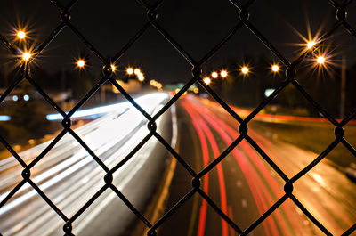 Close-up of illuminated chainlink fence against sky at night