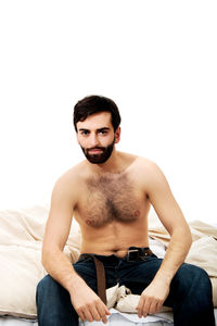 Portrait of young man sitting on bed against white background