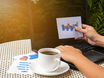 Cropped hand of woman using laptop by coffee on table