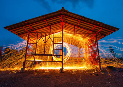 Illuminated wire wool under metallic structure against sky at night