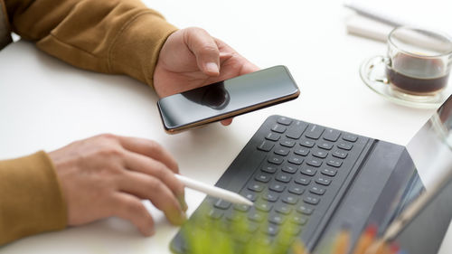 Cropped hands of person using laptop and phone on table