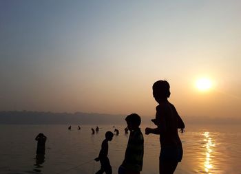 Silhouette men standing on beach against clear sky during sunset