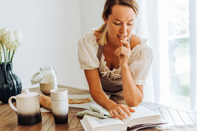 Woman reading a recipe book while cooking at kitchen