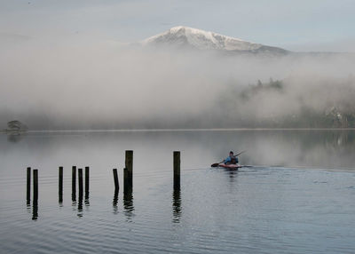 Man kayaking on lake against mountain during foggy weather