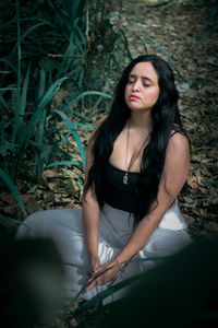 High angle view of woman with eyes closed mediating on land in forest