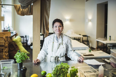 Portrait of confident mature female chef standing at kitchen counter in restaurant