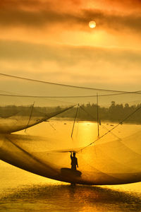 Silhouette man fishing in sea against sky during sunset