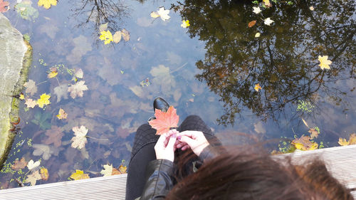 Low section of woman sitting on tree by water
