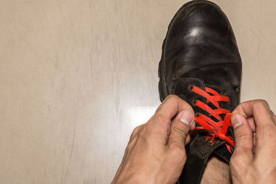 Cropped hand of man tying shoelace on floor