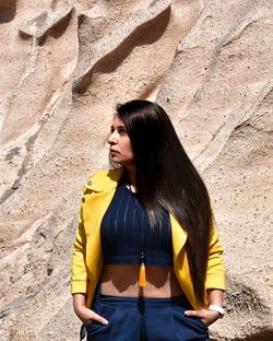 Young woman looking down while standing against yellow wall