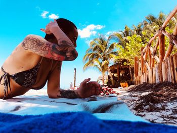 Side view of sensuous woman lying on picnic blanket at beach against sky