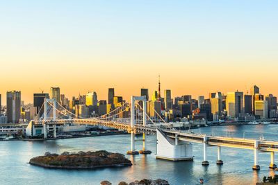 Bridge over river and buildings against sky during sunset