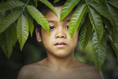 Close-up portrait of shirtless boy standing by plants