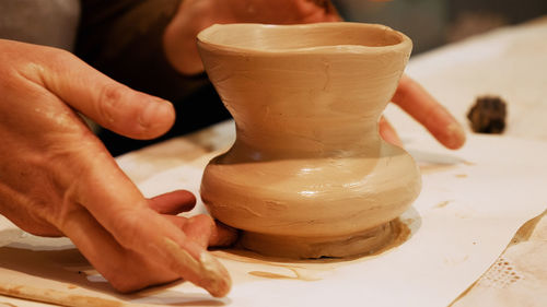 Cropped hands of craftsperson making clay product in pottery workshop