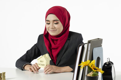 Portrait of smiling young woman holding red flowers against white background