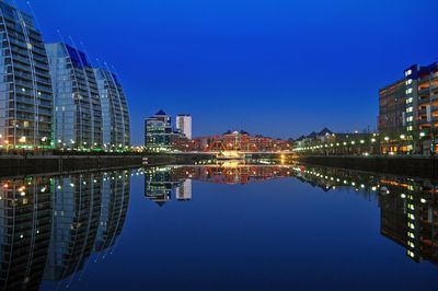 Illuminated buildings and bridge by calm lake at night