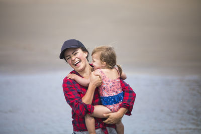 Mother laughing while holding baby girl at the beach.