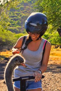 Smiling woman looking at ostrich against trees