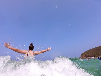 Rear view of woman splashing in sea against sky