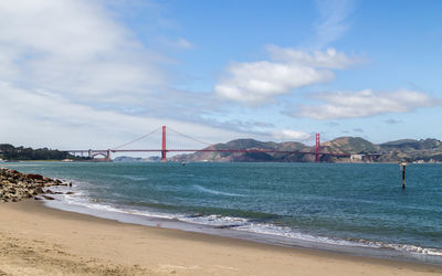 View of suspension bridge over sea against cloudy sky