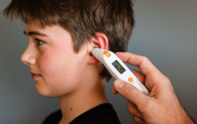 Tween boy getting temperature taken with an ear thermometer.