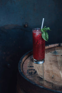 Strawberry basil drink in tall collins glass with paper drinking straw atop wooden barrel