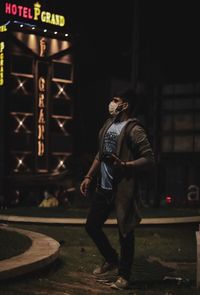 Full length of man standing against illuminated wall at night