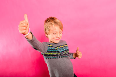 Smiling boy gesturing against pink wall