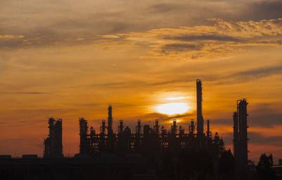 Silhouette factory against sky during sunset