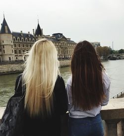 Rear view of women with long hair looking at historic building by river against sky