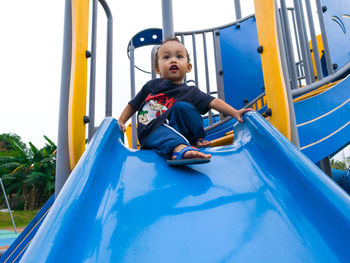 Cute boy sitting on slide in playground