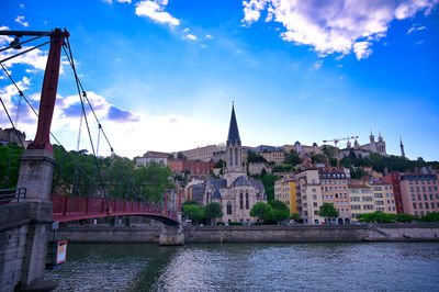 Bridge over river by buildings in city against sky