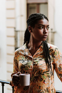 Young woman with cup of coffee standing on balcony