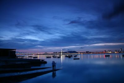 Silhouette men standing by lake against sky at dusk