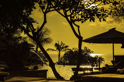 Silhouette trees by swimming pool against sky during sunset