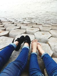 Low section of women sitting by sea