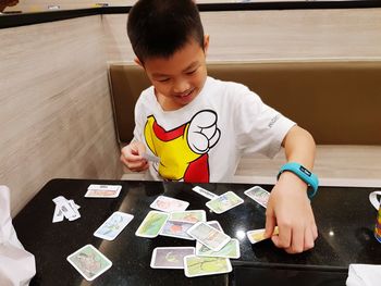 Cute boy playing cards at table in home