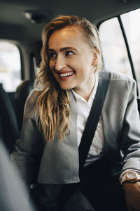 Smiling entrepreneur looking away while wearing seat belt in taxi