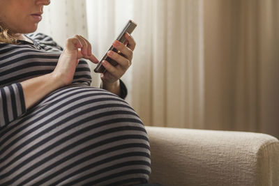 Midsection of man using mobile phone while sitting on sofa