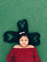 Girl with heart shape made of hair while lying on grassy field