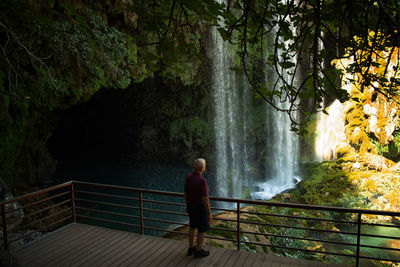 Rear view of man standing at observation point against waterfall