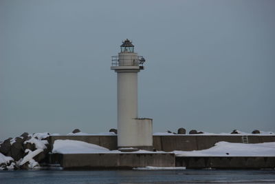 Lighthouse by sea against clear sky