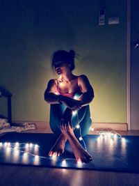 Young woman looking away while sitting on floor at home