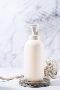 A minimalistic scene of a podium and white dispenser bottle with stones on white background