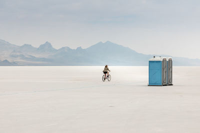 Woman cycling on salt flat against sky