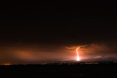 Lightning over silhouette cityscape against sky at night