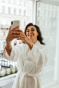 Smiling young woman video calling while standing at balcony