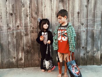 Siblings in costume standing against wooden wall during halloween