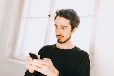 Portrait of young man using mobile phone at home