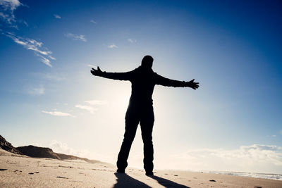 Silhouette man with arms outstretched standing at beach against sky